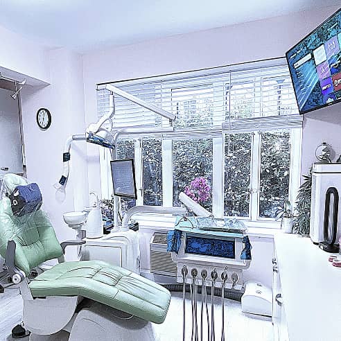 fifthavenuesmile | Color photo of a bright dental office with green chair, equipment, and large windows