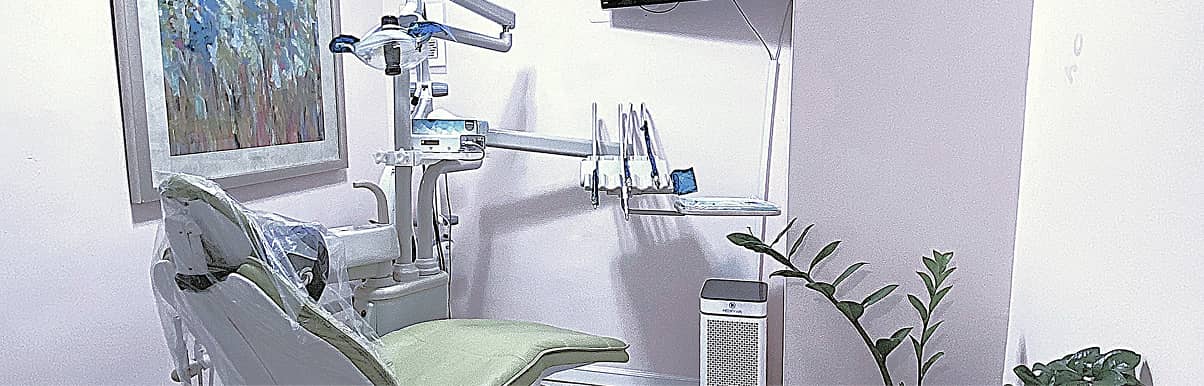 fifthavenuesmile | Dental treatment room with green chair, modern equipment, and framed artwork on the wall