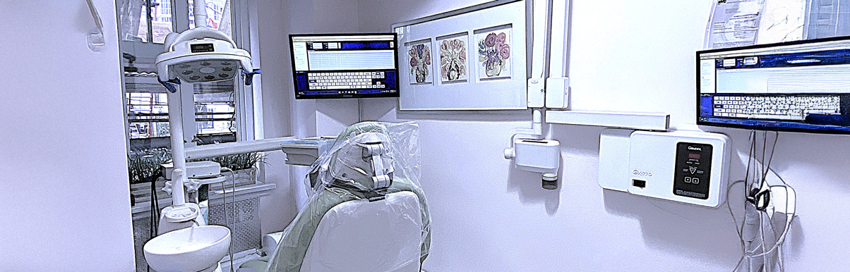fifthavenuesmile | Modern dental operatory with overhead exam light, computer monitors, dental chair wrapped in protective plastic, and framed artwork on the wall.