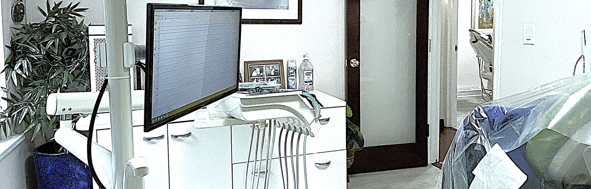 fifthavenuesmile | Dental treatment room with mounted monitor, dental instruments, cabinets, and a view into another operatory.