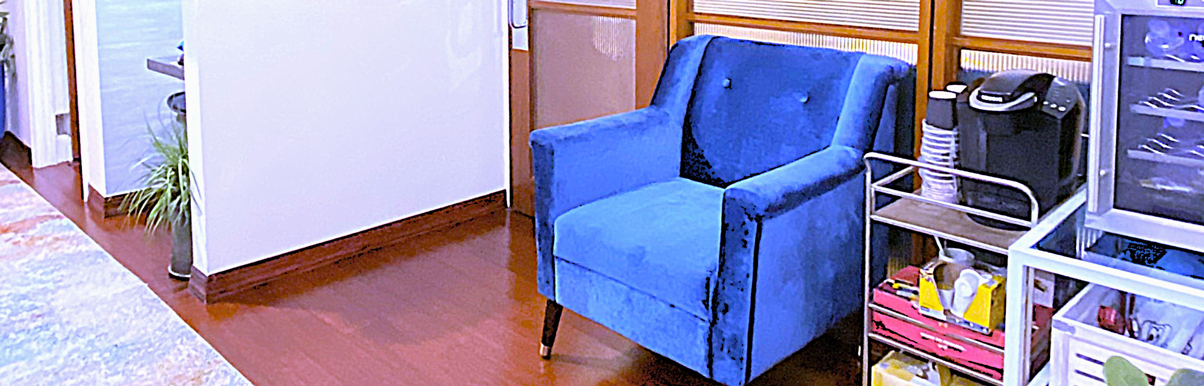 fifthavenuesmile | Waiting area corner with plush blue armchair, hardwood floor, small beverage station with coffee machine, and supply cart.