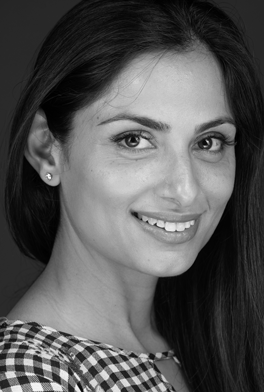 fifthavenuesmile | Black and white headshot of a smiling woman with long hair, wearing a checkered top and stud earrings.